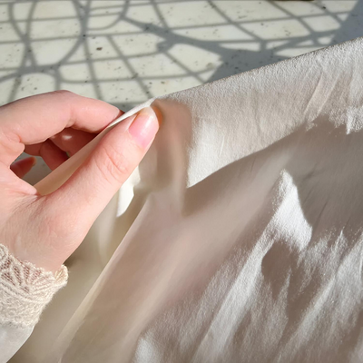 Hand holding a piece of light-colored fabric with a textured surface.